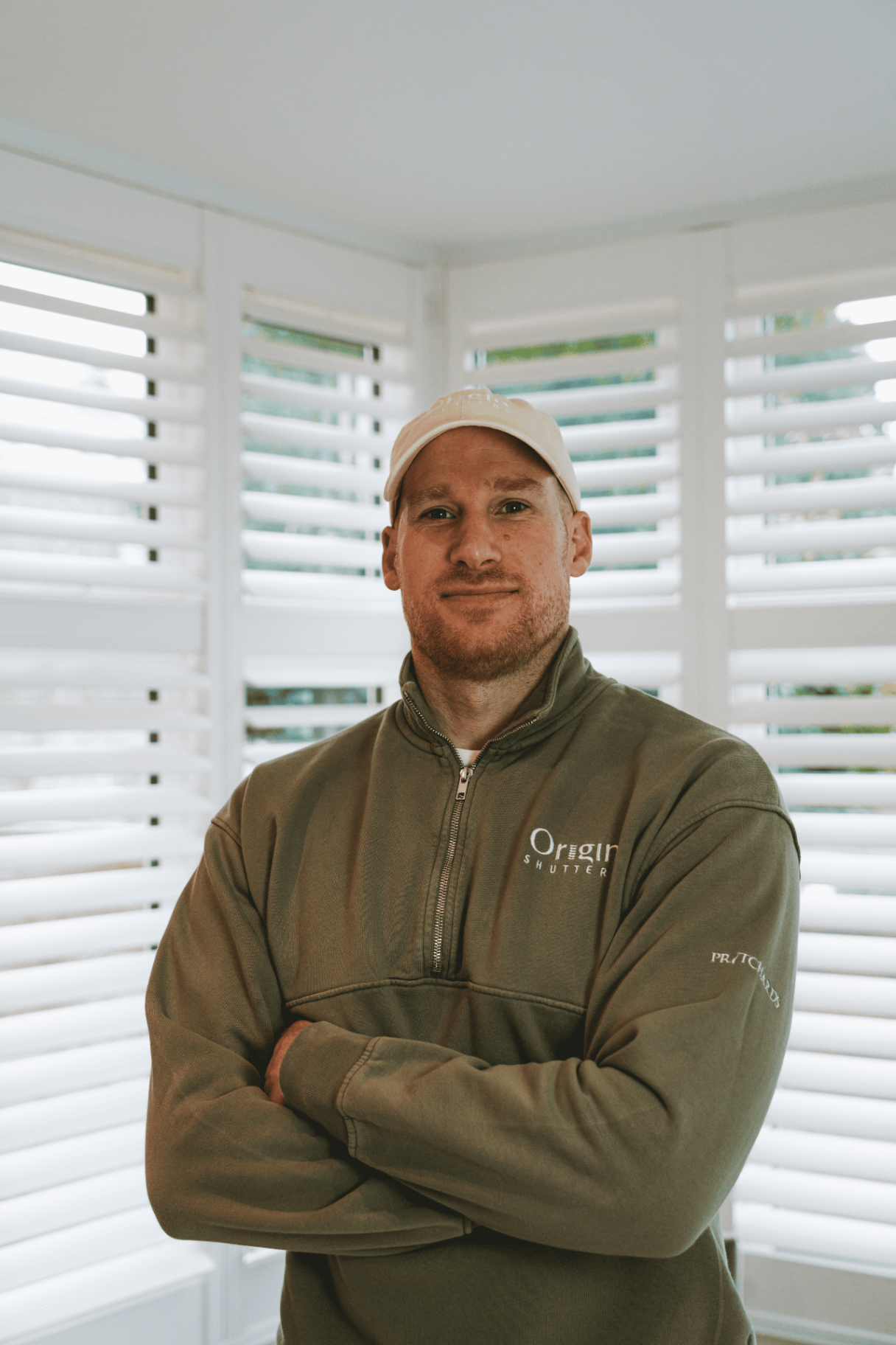 Sam from Origin Shutters wearing branded workwear with arms folded in front of fitted shutters