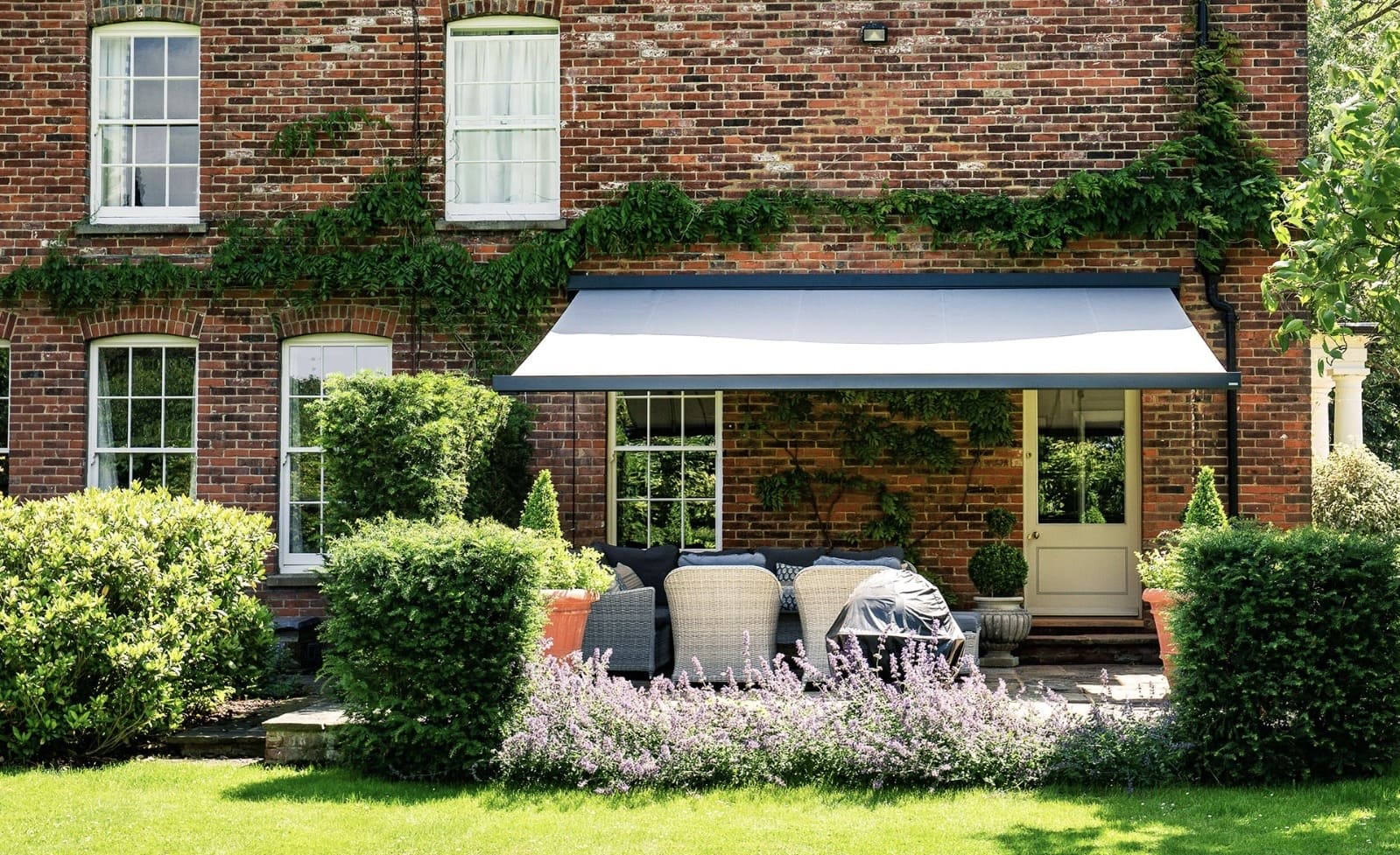 Large grey and white retractable awning over garden seating at a period red brick manor house