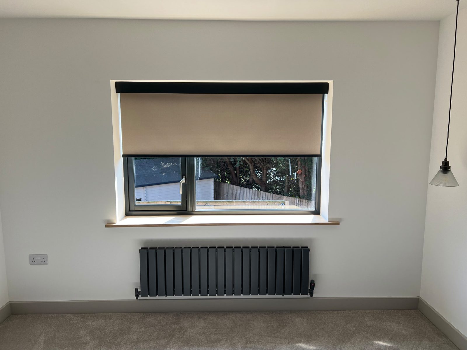 Single neutral roller blind fitted above a radiator in a bright room
