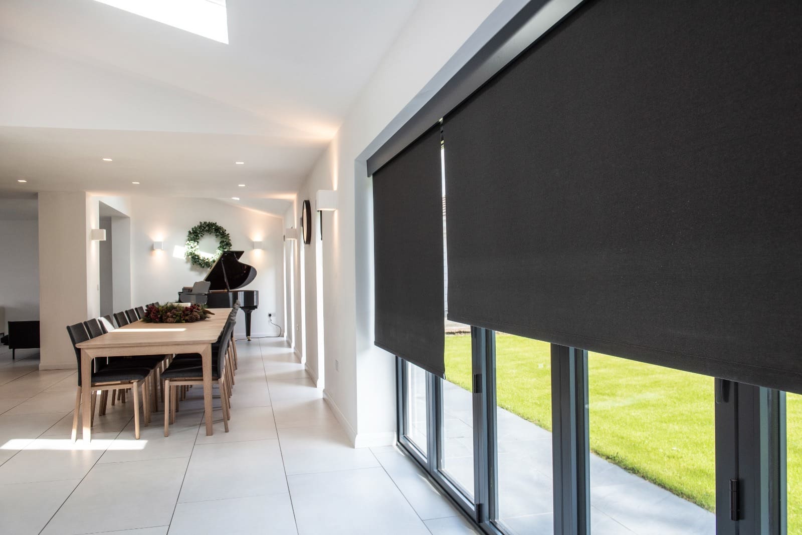 Black roller blind in a grand white dining room with a long table and piano