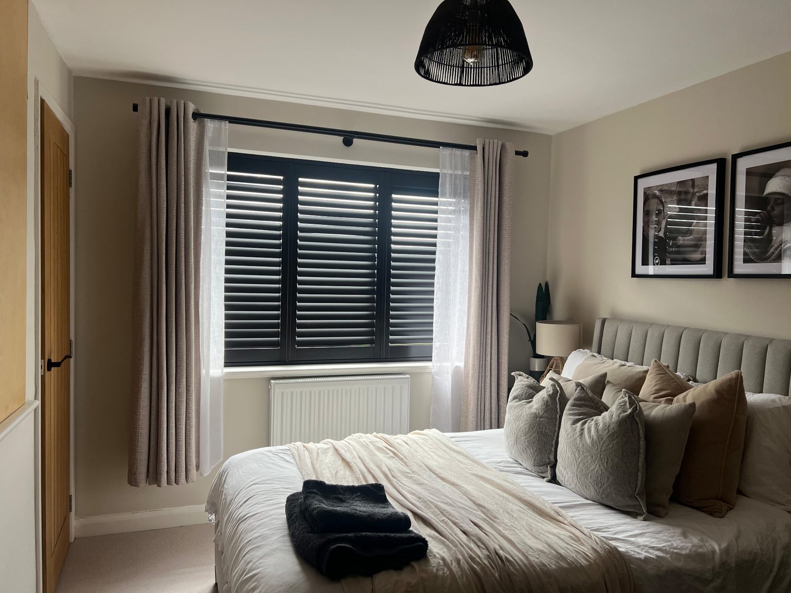 Black plantation shutters closed across a bedroom window framed by curtains