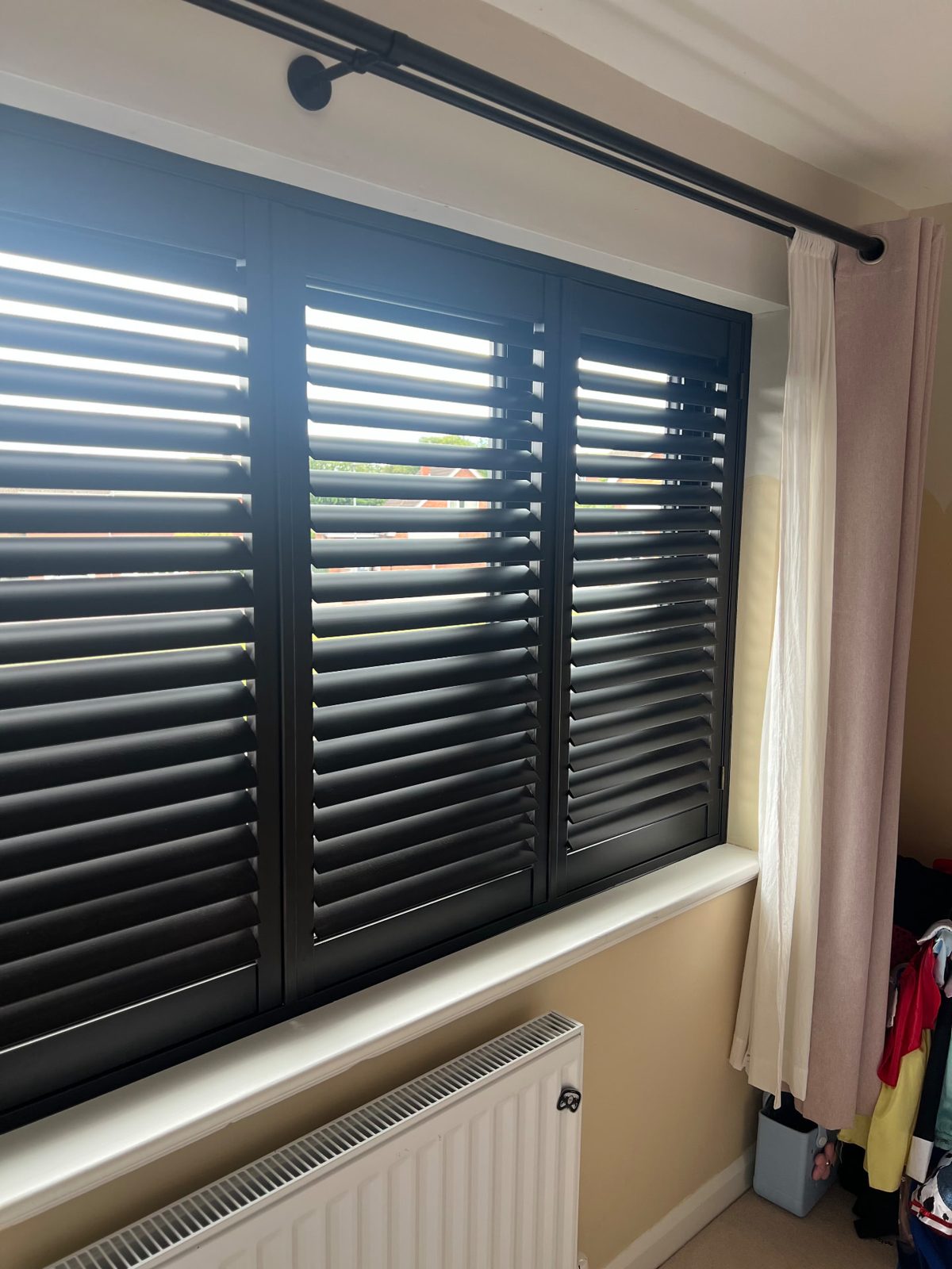 Dark grey plantation shutters fitted inside a window reveal above a radiator