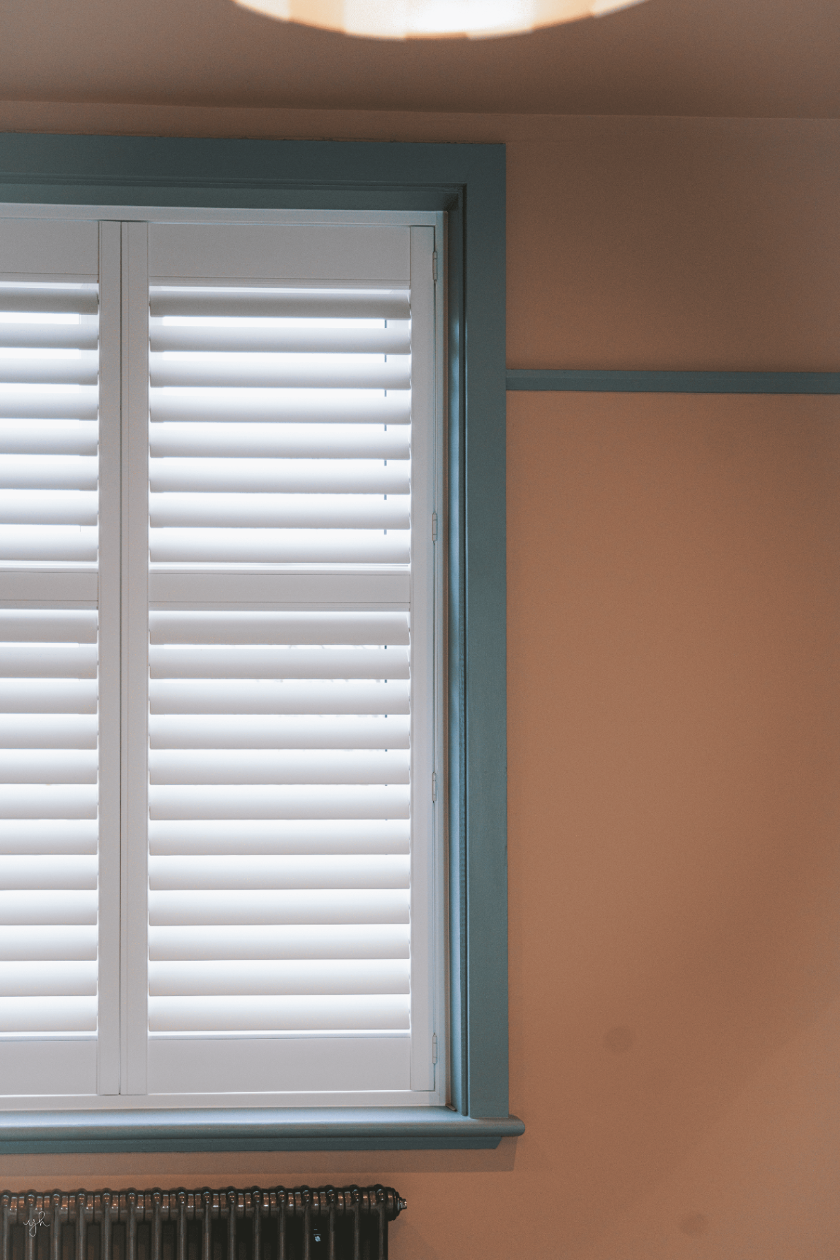 White shutters fitted within a coloured frame above a cast iron radiator
