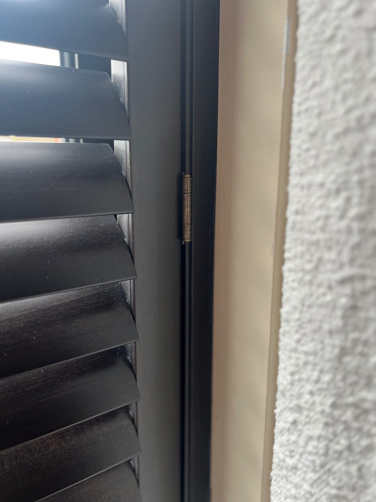 Close-up of a dark wood shutter panel showing the hinge and frame detail