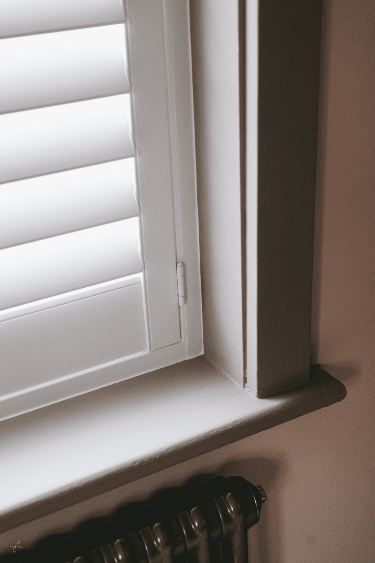 Hinge and sill detail of white shutters fitted inside a window reveal