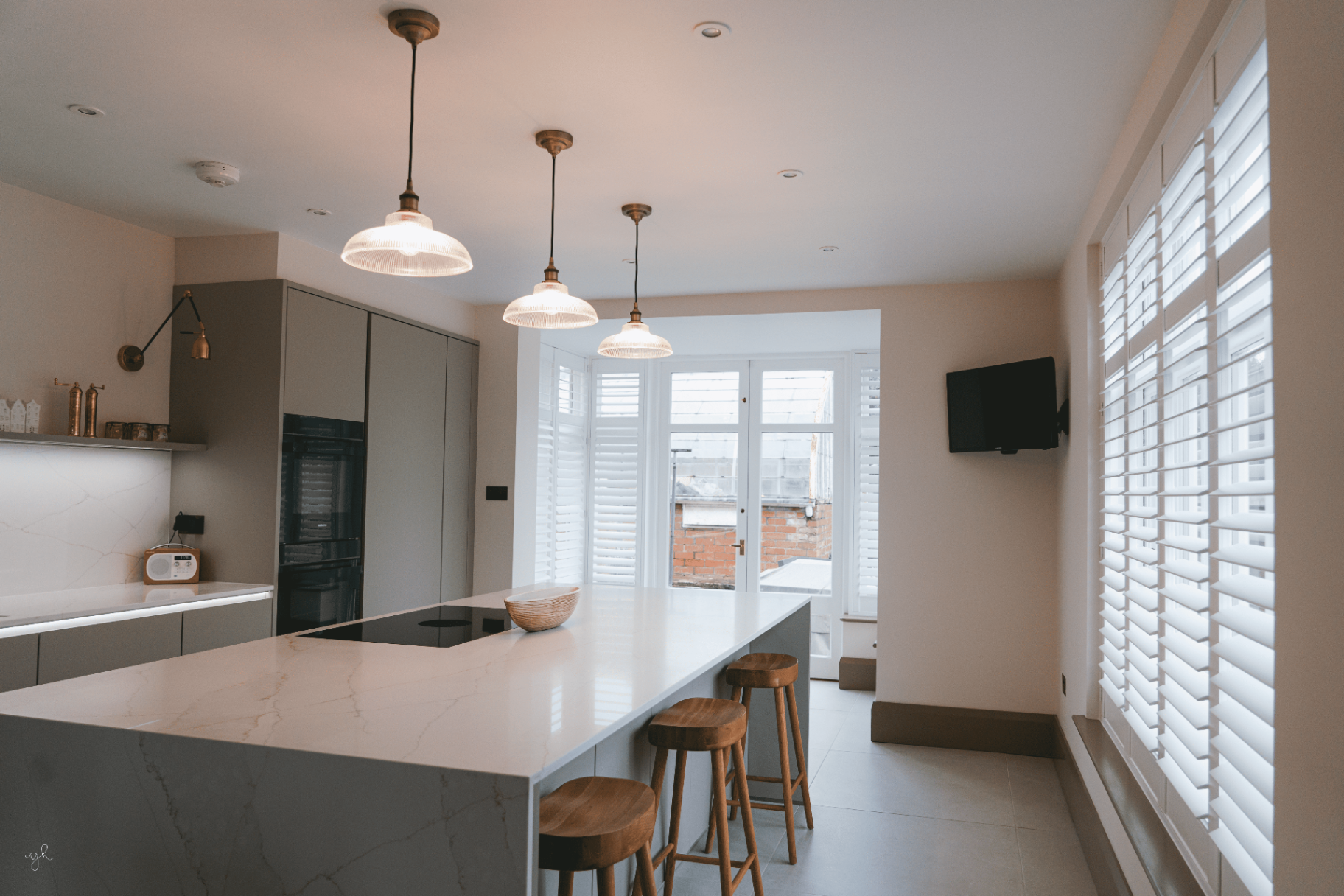 Full height shutters fitted on two walls of a modern kitchen with a marble island