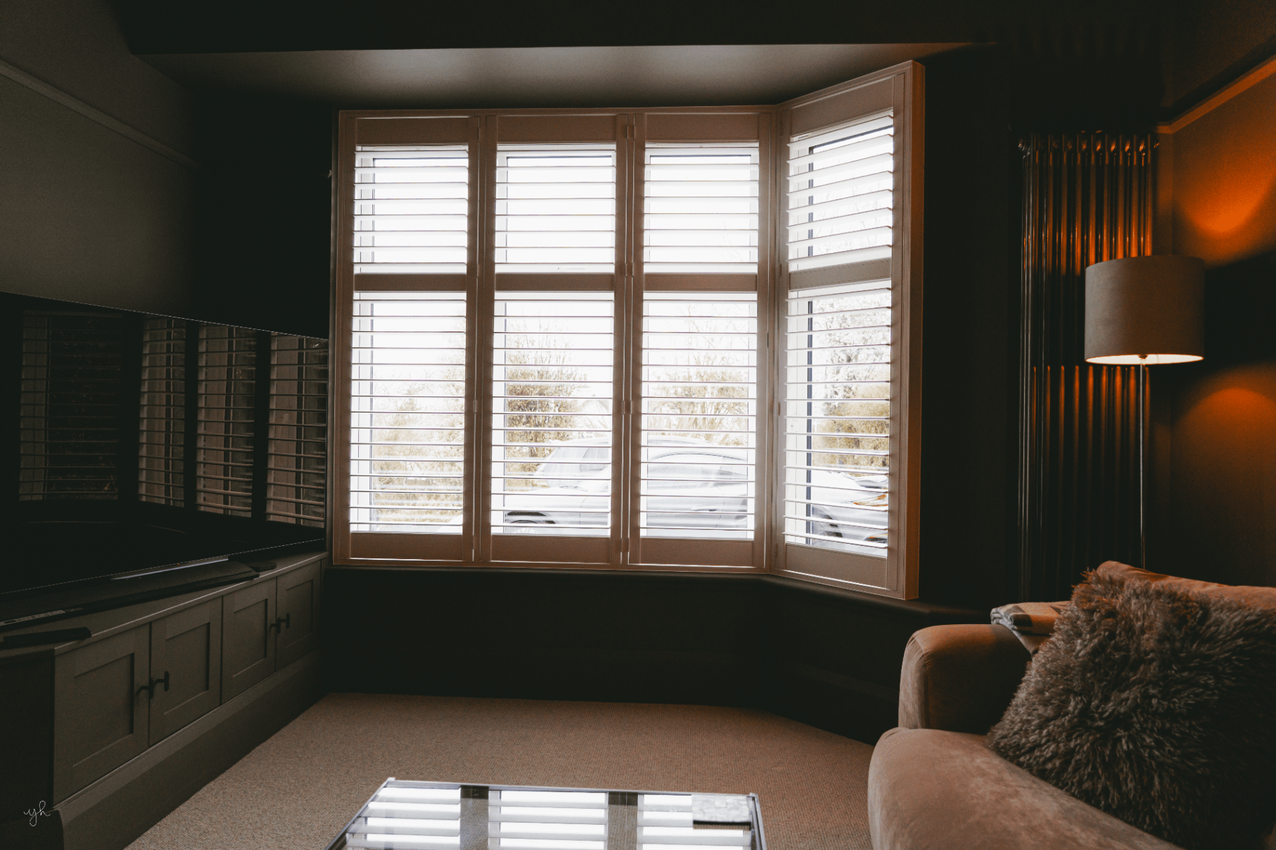 Wooden bay window shutters in a dark moody living room with a floor lamp