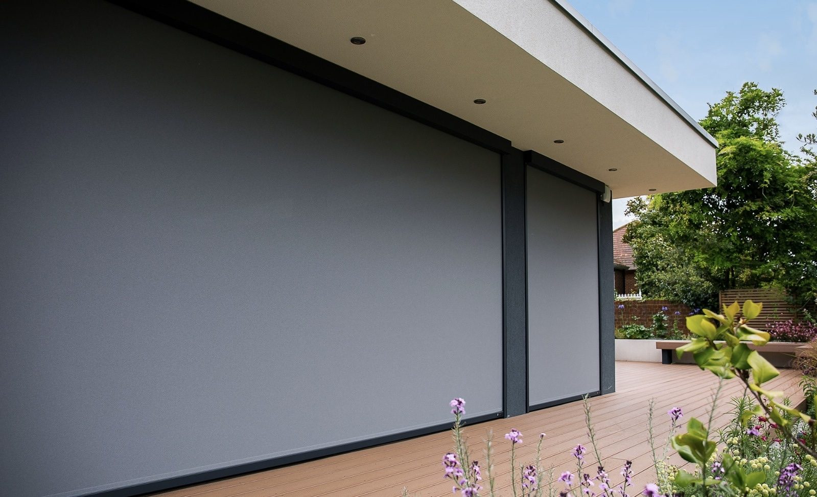 Anthracite exterior zip screens lowered over large glass doors beside a timber deck